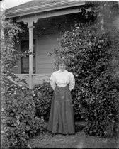 Woman posing in front of Victorian home with vines, c. 1912
