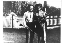 Snort Van Art and George Rhea standing in front of a white picket fence and holding rifles
