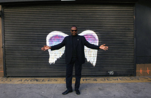 Unidentified man with sunglasses posing in front of a mural depicting angel wings