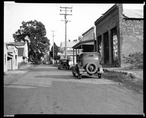 View of an unidentified street in Fiddletown, showing parked cars and a Mobil gas station, 1936
