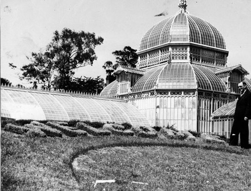 [Unidentified man standing next to floral display in front of the Conservatory of Flowers in Golden Gate Park]