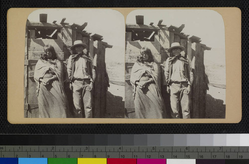A native man and woman, most likely Hualapai, stand in front of a wooden shelter