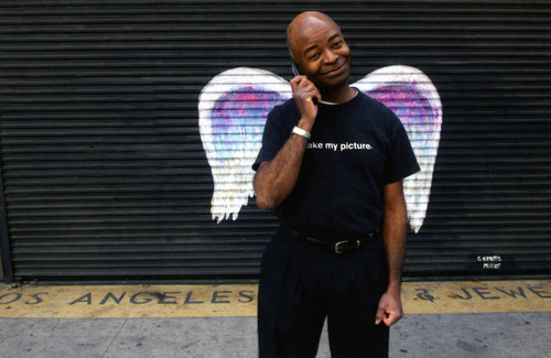 Unidentified man with cell phone posing in front of a mural depicting angel wings