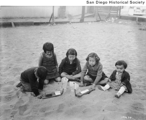 Five Japanese children playing in a large sandbox