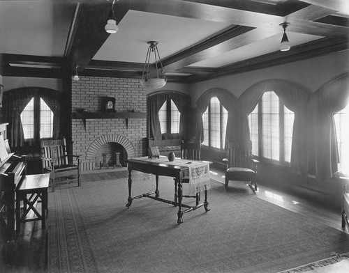 View of living room with piano and table in center and fireplace at the far end