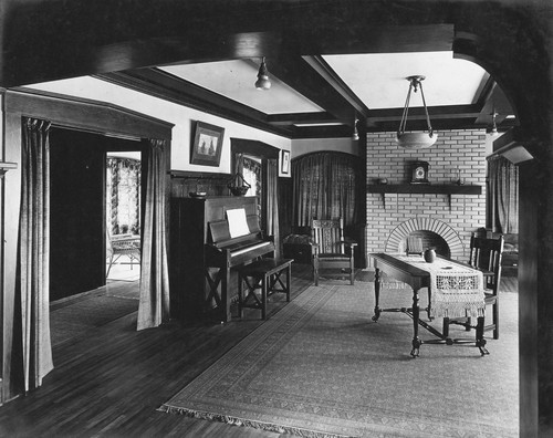 View of living room with piano and table in center and fireplace at the far end