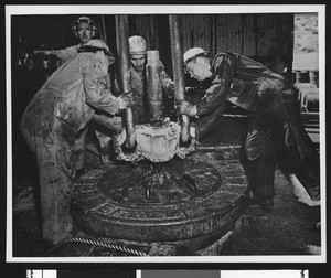 Men working around a cylindrical object in an oil refinery, ca.1940