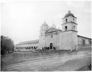 General view of the Mission Santa Barbara, with people on the front steps of the church, ca.1897-1898