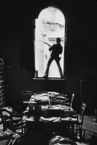 Sandinista standsing on sill of broken window, Nicaragua, 1979