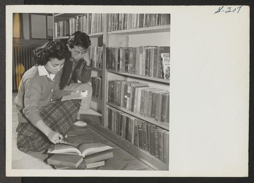 Scene in the Heart Mountain High School library, as Miss Mickey Yabe helps a fellow student with some research work in ancient history. Photographer: Iwasaki, Hikaru Heart Mountain, Wyoming