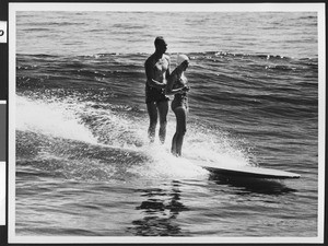Man and woman sharing a surfboard, ca.1950