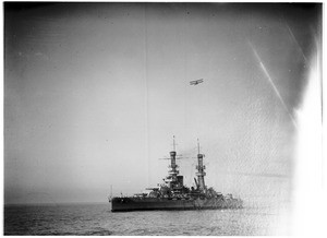 Biplane flying over a battleship at sea