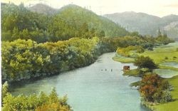 Scene of the Russian River surrounded by mountains and redwoods, about early 1900s