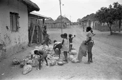 Small children pick up large boulders next to a building, San Basilio de Palenque, 1977