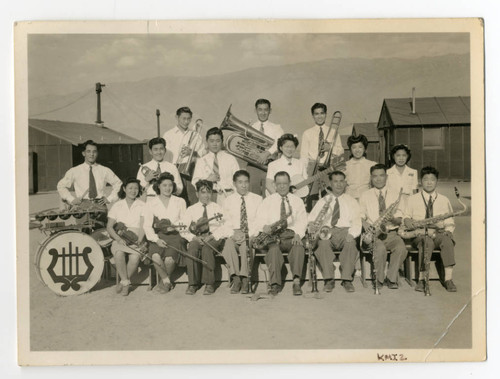 Photograph of a musical group at Manzanar posed in front several buildings with the Inyo Mountains in the background