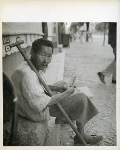 Man sitting on sidewalk with cane