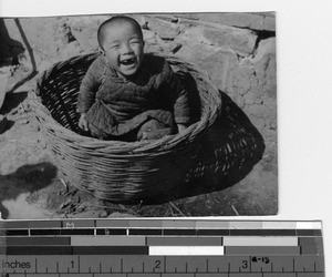 A happy baby in a basket at Luoding, China, ca.1930