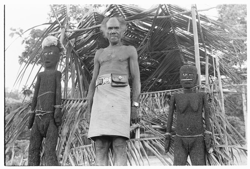 Folofo'u, wearing old police belt, on speaking platform with fernwood 'ea figures made by Arimae of Furi'ilae for the opening of the Kwaio Cultural Centre in August 1979