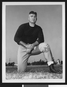 University of Southern California assistant football coach Ray George, wearing dark sweatshirt and posing on one knee, Bovard Field, 1949