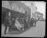 People riding boardwalk trolley as it passes auction house and Neptune Theatre in Venice, Calif., circa 1925