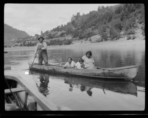 Pete Williams standing in canoe with two women and a child - Yurok