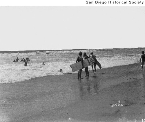 People swimming and standing with surfboards on beach in Del Mar