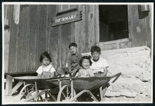 Photograph of Ned and Harry Morioka with two other children posing in front of the infirmary at Cow Creek Camp in Death Valley