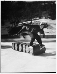 Two men in ice skates leaping over a line of barrels at Big Pines