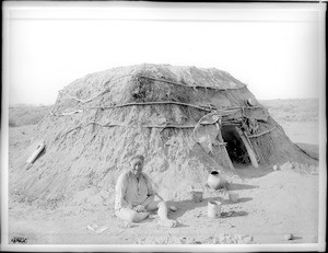 Pima Indian man, Ho-Dutch, sitting in front of his native dwelling, or "Kan", Pima, Arizona, ca.1900