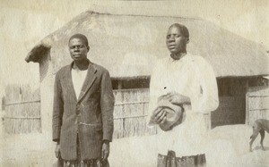Two African men : Nalumino and Josefa. Behind them, one of their house