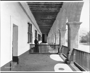 Outdoor corridor with a monk at Mission Santa Barbara, 1898