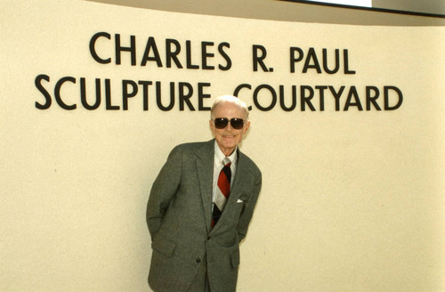 Charles R. Paul standing in front of the sign "Charles R. Paul Sculpture Courtyard"