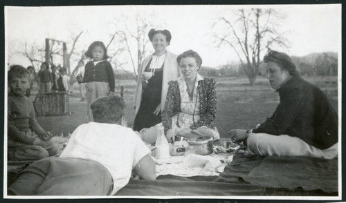 Photograph of a group of people enjoying Sunday dinner as a picnic at Manzanar