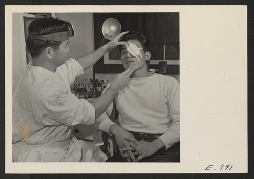 Dr. Nobuo Renge applies an eye bandage to George Arita in the center hospital clinic. All functions of the hospital are performed by center residents (former west coast persons of Japanese ancestry), except for the chief doctor and the superintending nurses. Photographer: Parker, Tom Denson, Arkansas