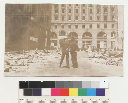 [Two men conversing among ruins on New Montgomery St. Market St. in distance. Palace Hotel, left.]