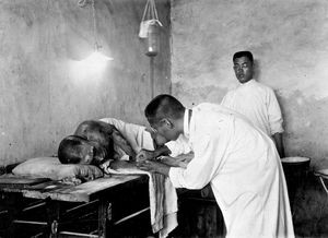 Fra koleraepidemien i Antung 1919. Det store tempel tæt ved hospitalet blev overladt missionslægerne til nødhospital. Epidemien blev ret hurtigt bekæmpet. Her får en hårdt medtaget patient saltvandsindsprøjtning