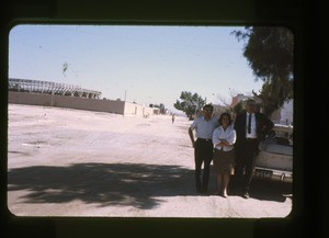 two men and one woman standing beside an automobile on a city street