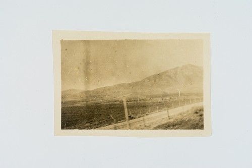 Unidentified image of dirt road in front of a field with mountain in background