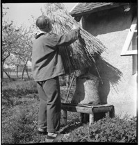 [Artist / sculptor Henri Edouard Navarre with straw thatch and bell-shaped ceramic outside country cottage and ceramics studio]