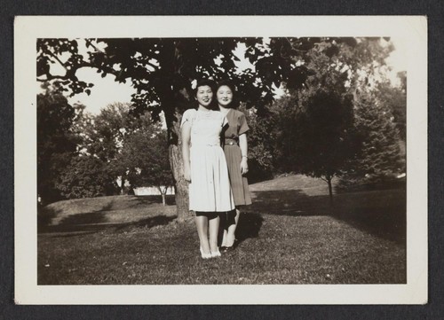 [two young women standing under tree]