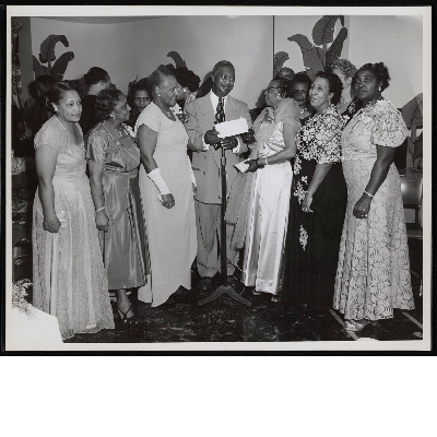 B.F. McLaurin standing at microphone handing envelope to group of women