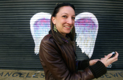 Unidentified woman holding cell phone posing in front of a mural depicting angel wings