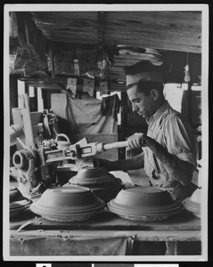 Worker applying a tool to a clay-like material, ca.1930