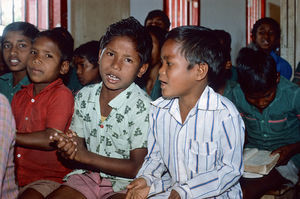 Diasserie for børn: "En dag på Saraswatipur Kostskole"- Nr. 45. Bidhan er for lille til at spille trommer. Men han kan til gengæld synge både højt og flot, og det gør han - "Abar deka hobe" - Vi ses en anden gang!