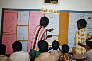 39.- Tamil Nadu, Indien, 1988-89. "Med 80 elever i klassen" - En dansk lærer i Arcot skoleprojekt fortæller: Når oplysninger var færdigbehandlet, blev plancher hængt op på opslagstavlen, så alle elever kunne se, hvad der var kommet ud af det, og hvad de andre grupper havde fundet ud af. Det blev også brugt i aftenskolen. Eleverne kunne der fortælle deres forældre og de børn, der kom om aftenen, hvad de havde lavet. Til venstre ses, hvor mange mænd og kvinder, muslimer, hinduer og kristne, der er i landsbyen, ligesom man kan se noget om aldersfordelingen. Til højre på opslagstavlen kan man se noget om, hvor gamle husene er og lidt om husdyrholdet