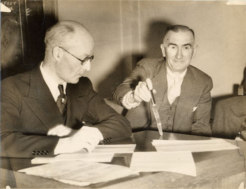[Inspector Allen McGinn (right), seated with unidentified man and holding a knife]