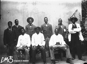 Group of African men sitting and standing in rows in front of a building, Antioka, Mozambique, ca. 1901-1915