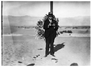 Old man reading from a Bible in front of a cross at a funeral in the desert