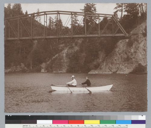 Two men in rowboat, railroad bridge in background, Bohemian Grove. [photographic print]
