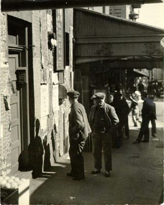 [Two men reading notices pasted to the walls of a building in Chinatown]